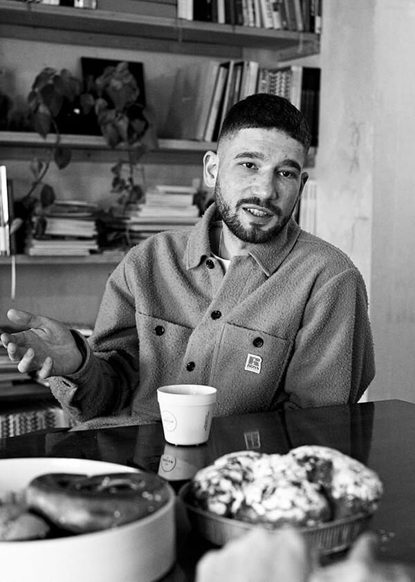 Black and white photo of a person sitting on a table next to some of food.