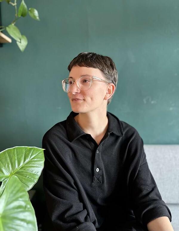 a woman sitting on a couch framed by plant leaves